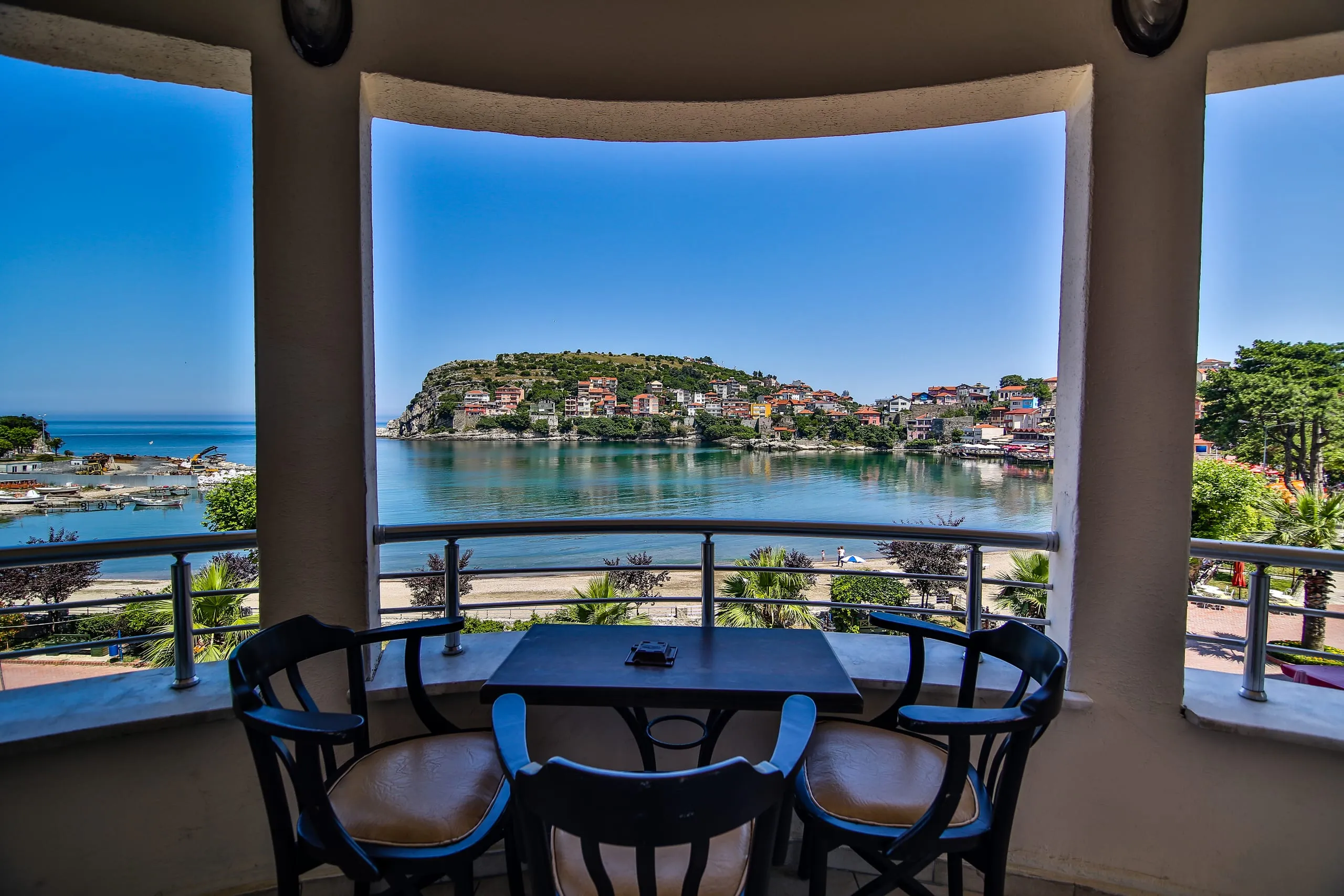 Aile Odası balkonundan Amasra koyu; kemerli balkon açıklığı manzarayı çerçeveliyor, önde masa ve sandalyeler
