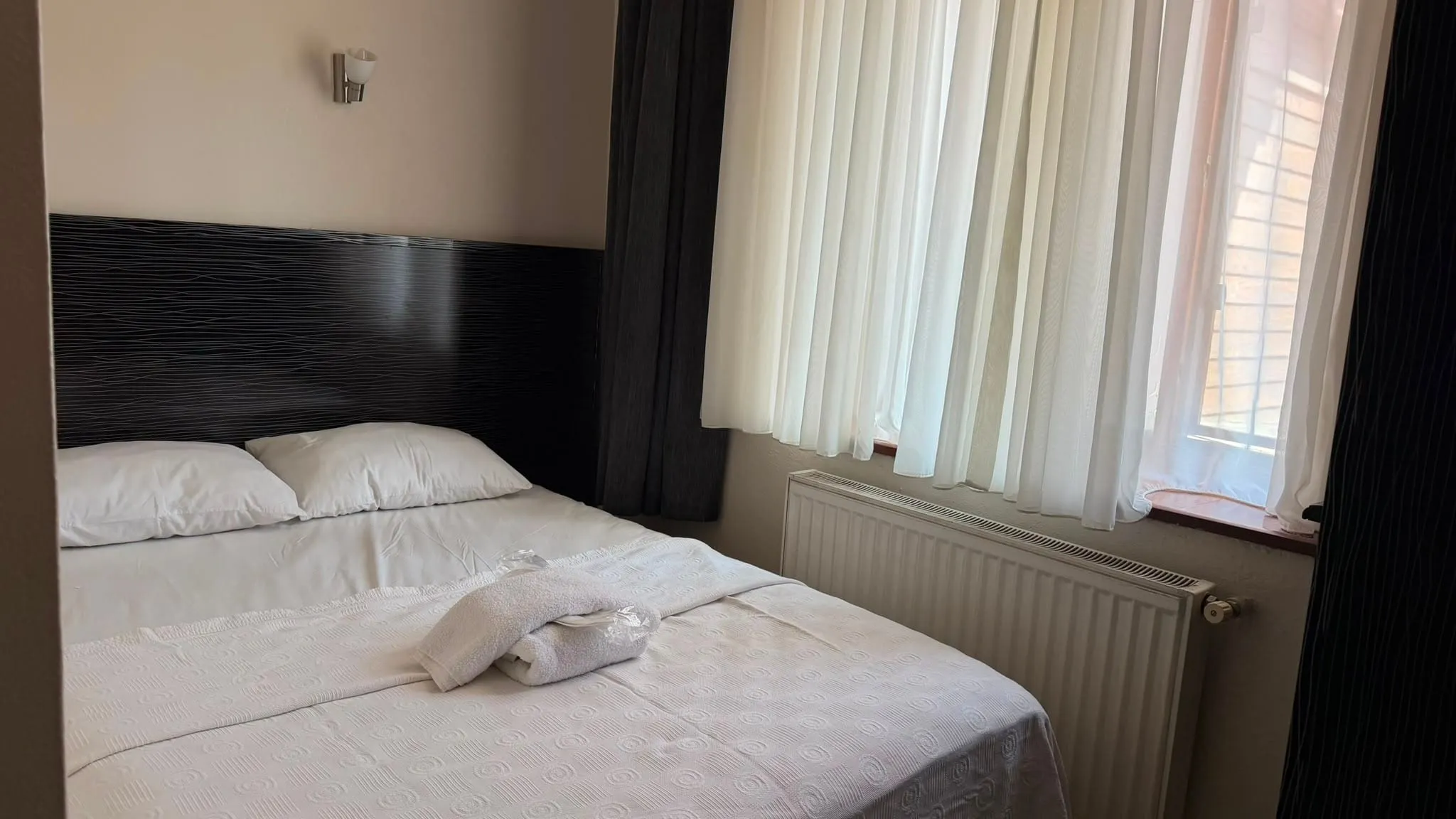 Aile odasında hazırlanmış çift kişilik yatak, katlanmış havlular ve tüllü pencere