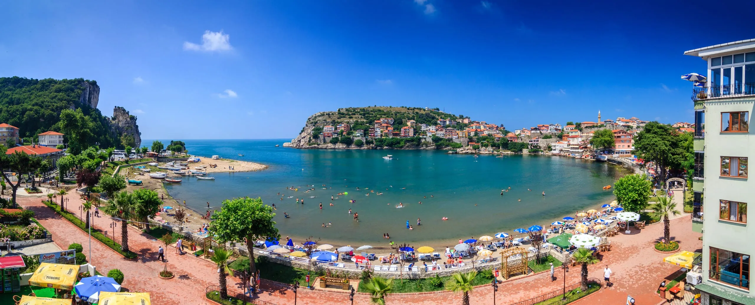 Amasra'da hilal biçimli koy: kumsal, şemsiyeli sahil promenadı ve arkada yarımadadaki tarihi Amasra evleri