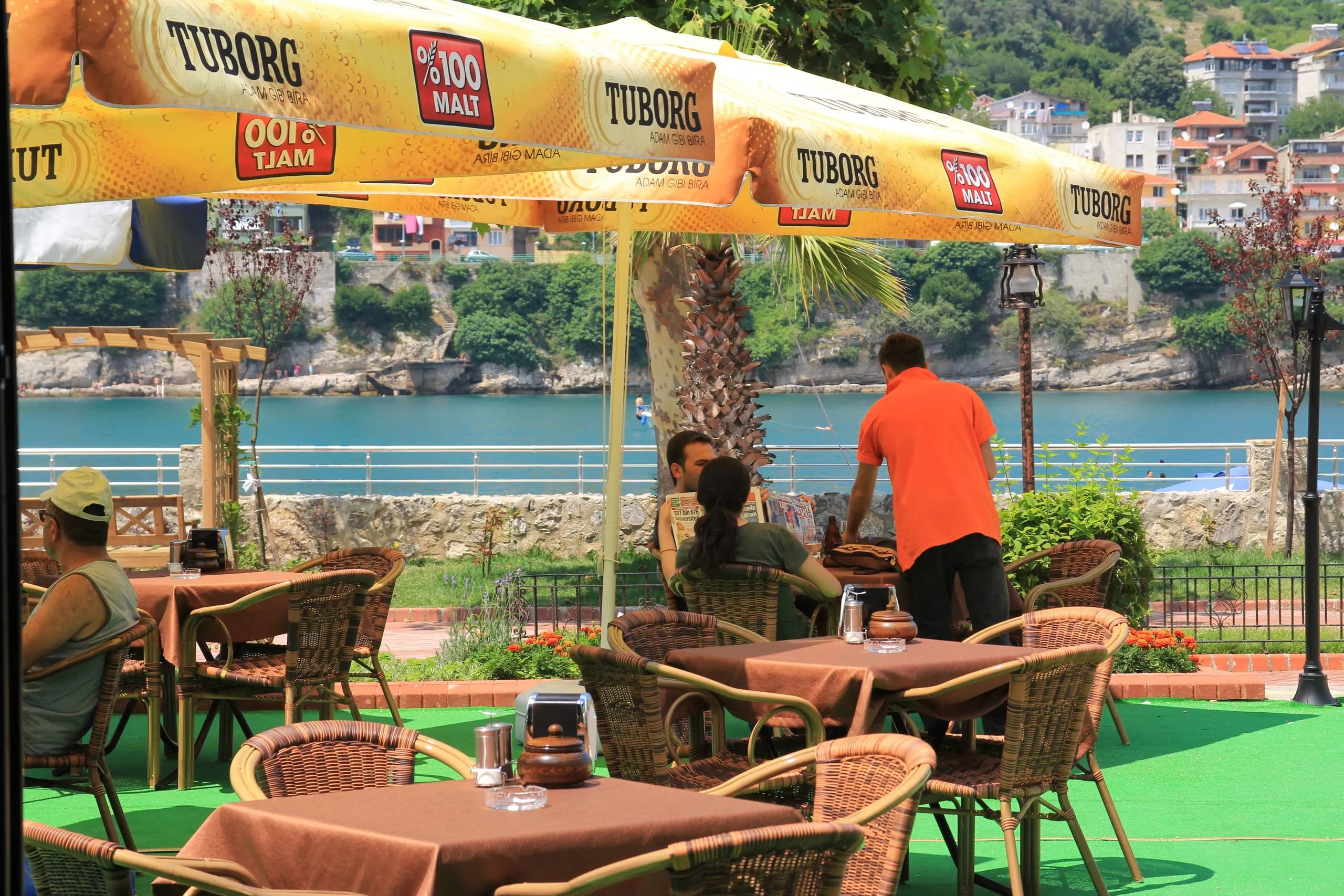 Özgün Cafe'nin denize bakan açık hava terası; hasır sandalyeli masalar ve arkada Amasra koyu