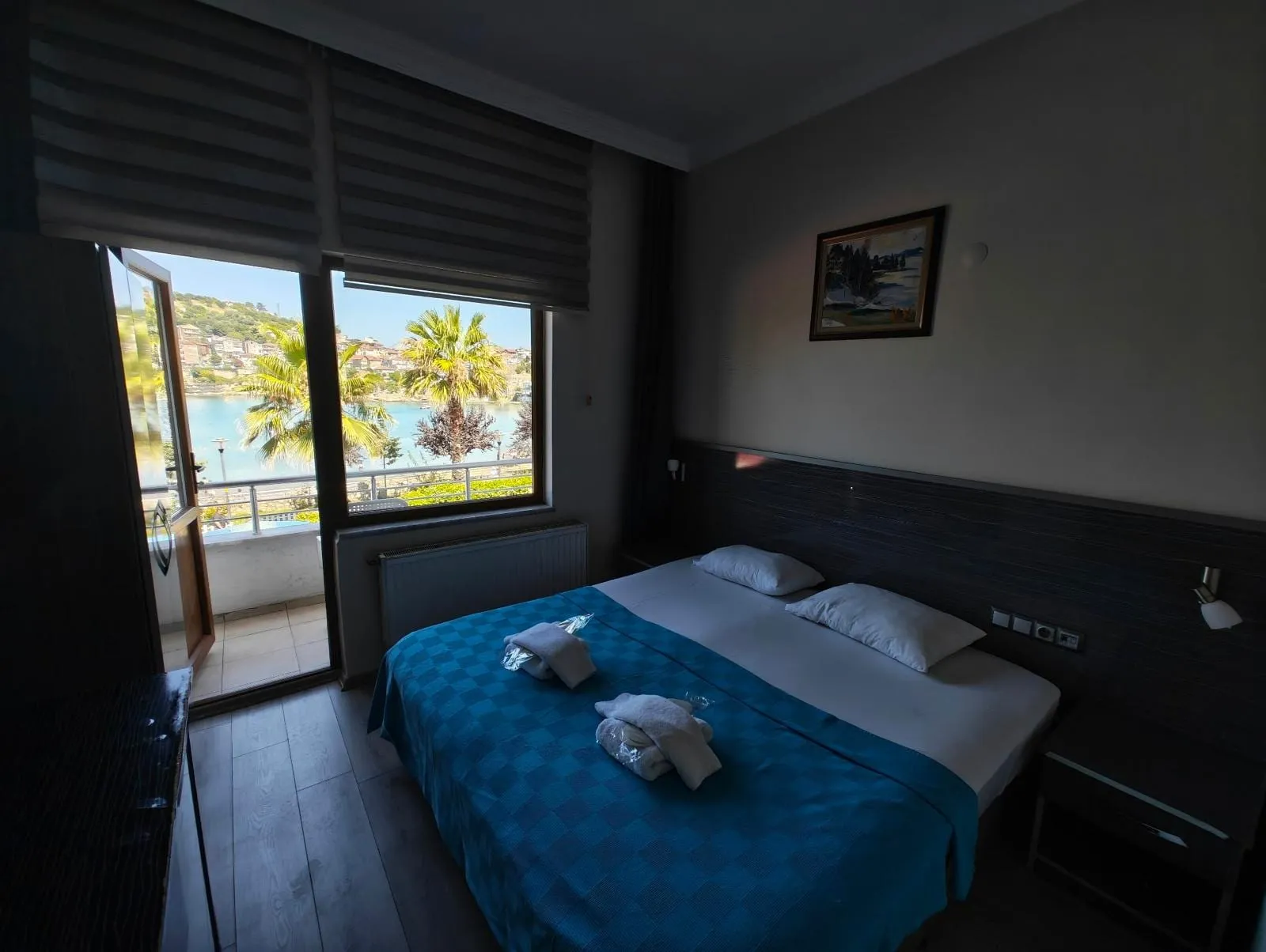 Lüks oda: turkuaz örtülü çift yatak ve balkon kapısından görünen Amasra koyu