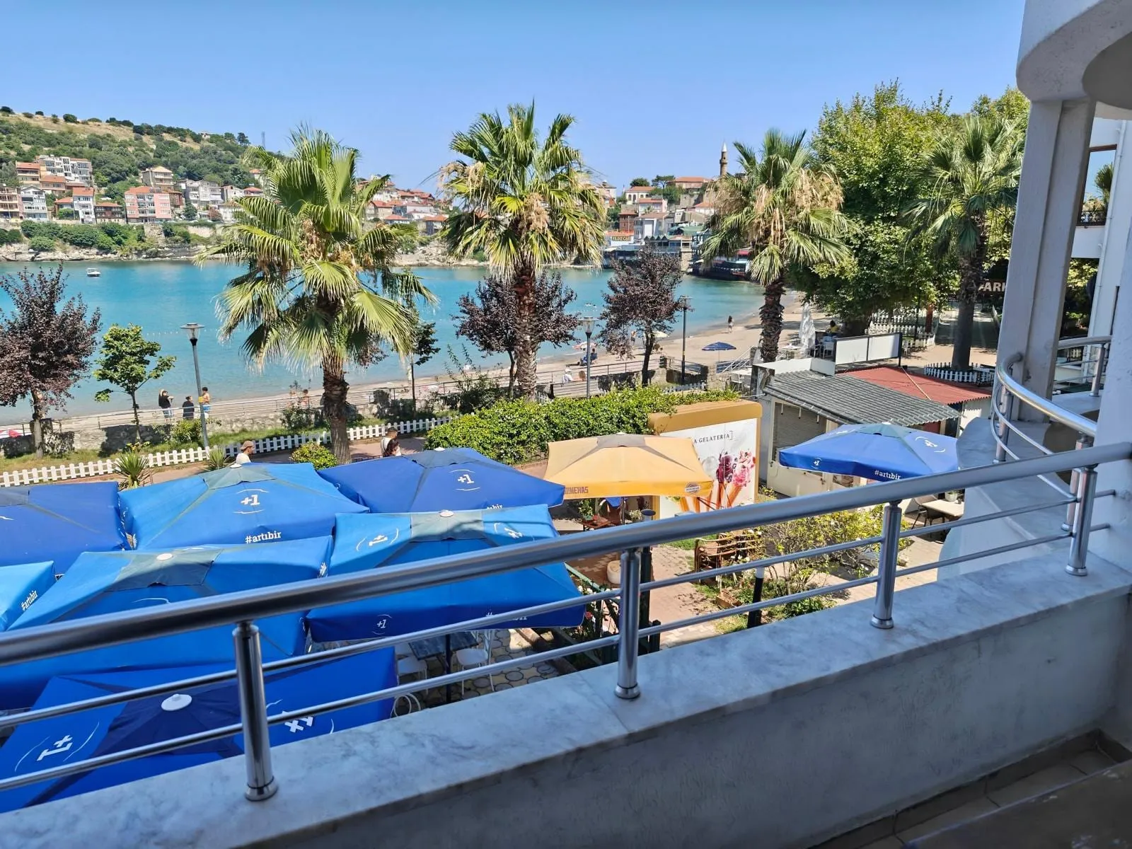 Lüks odanın balkonundan Amasra koyu: palmiyeler, sahildeki şemsiyeler ve karşı yamaç