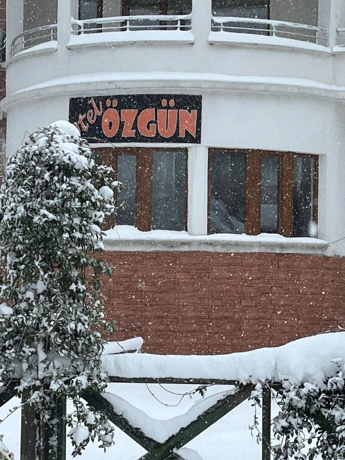 Kar yağarken 'Otel Özgün' tabelası ve karla kaplı sarmaşık