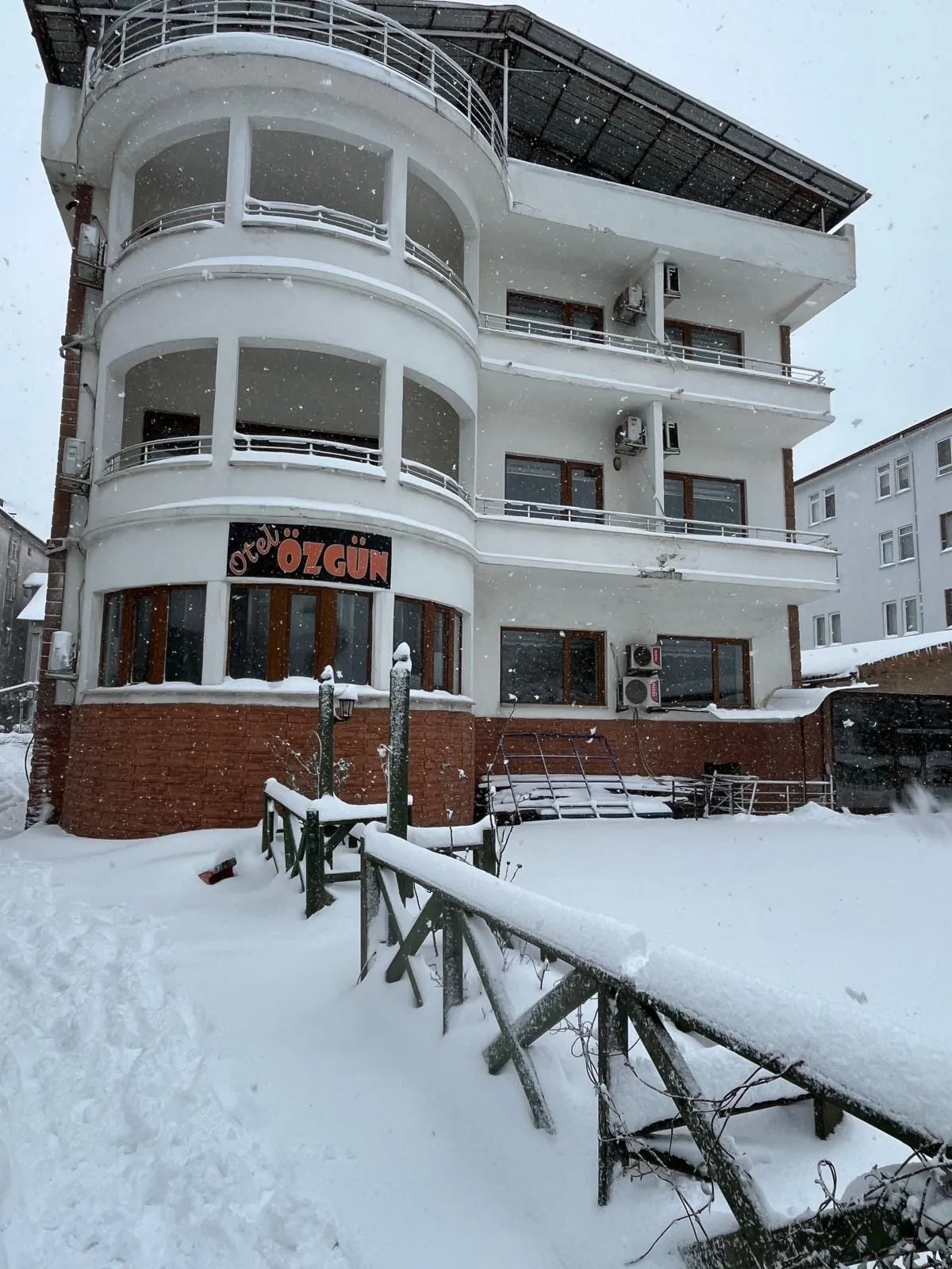 Kar altında Amasra Özgün Otel binası: kavisli balkonlar ve karla kaplı bahçe