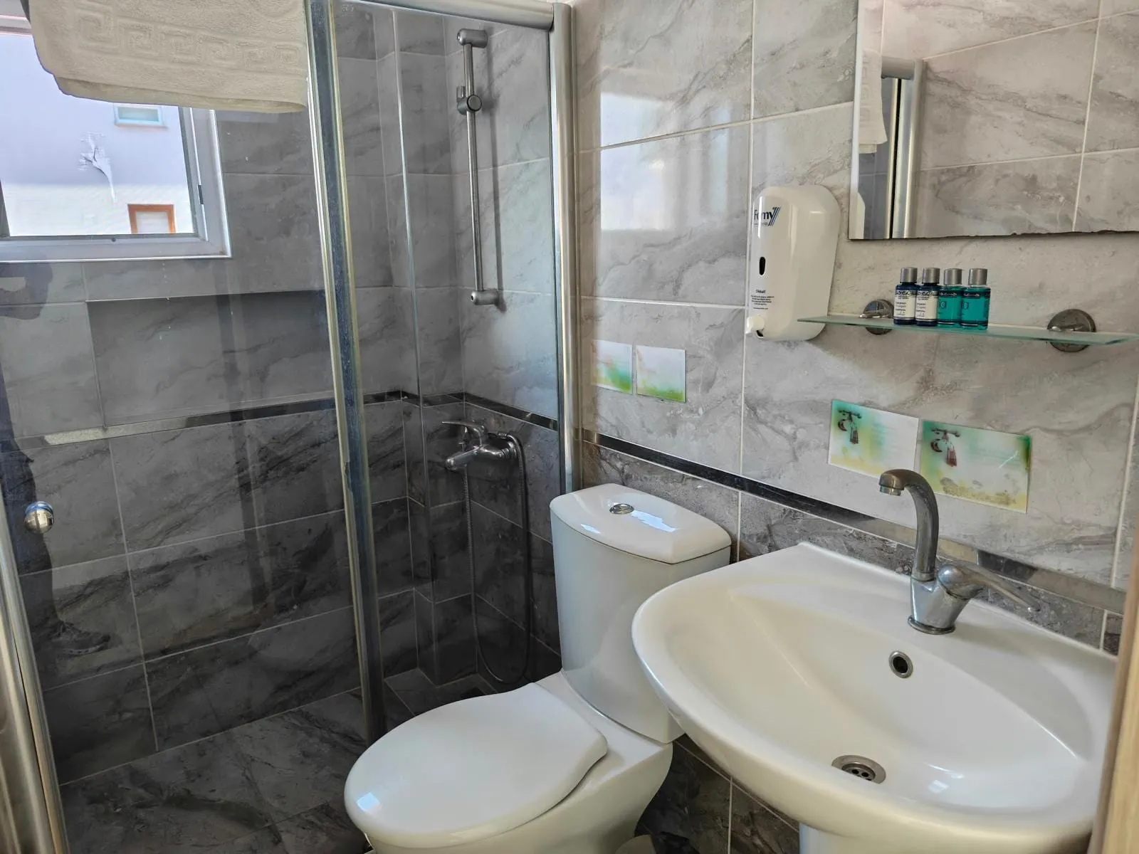 Standart oda banyosu: cam duşakabin, lavabo ve mermer desenli duvar