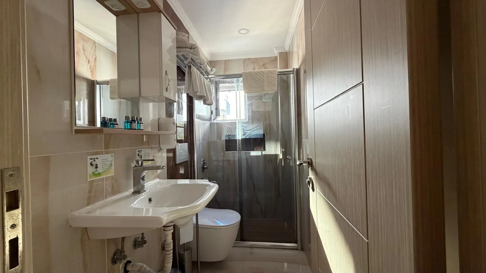 Standart oda banyosu: lavabo, ayna, duşakabin ve ahşap dolap